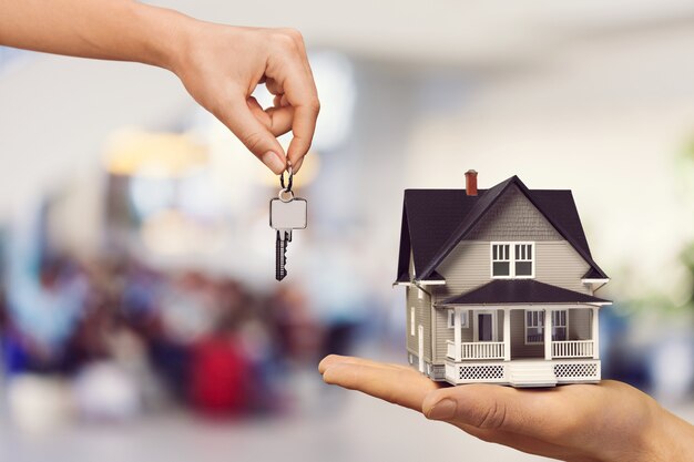 Hand holding a miniature house while another hand offers keys, symbolizing buying, selling, or renting a new home.
